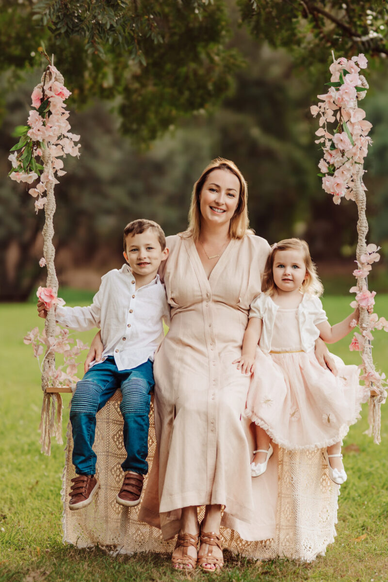 Niamh sitting with two children on a swing dressed with florals.